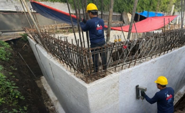 An INTRIC crew fastening bentonite geotextile to a foundation wall before backfill